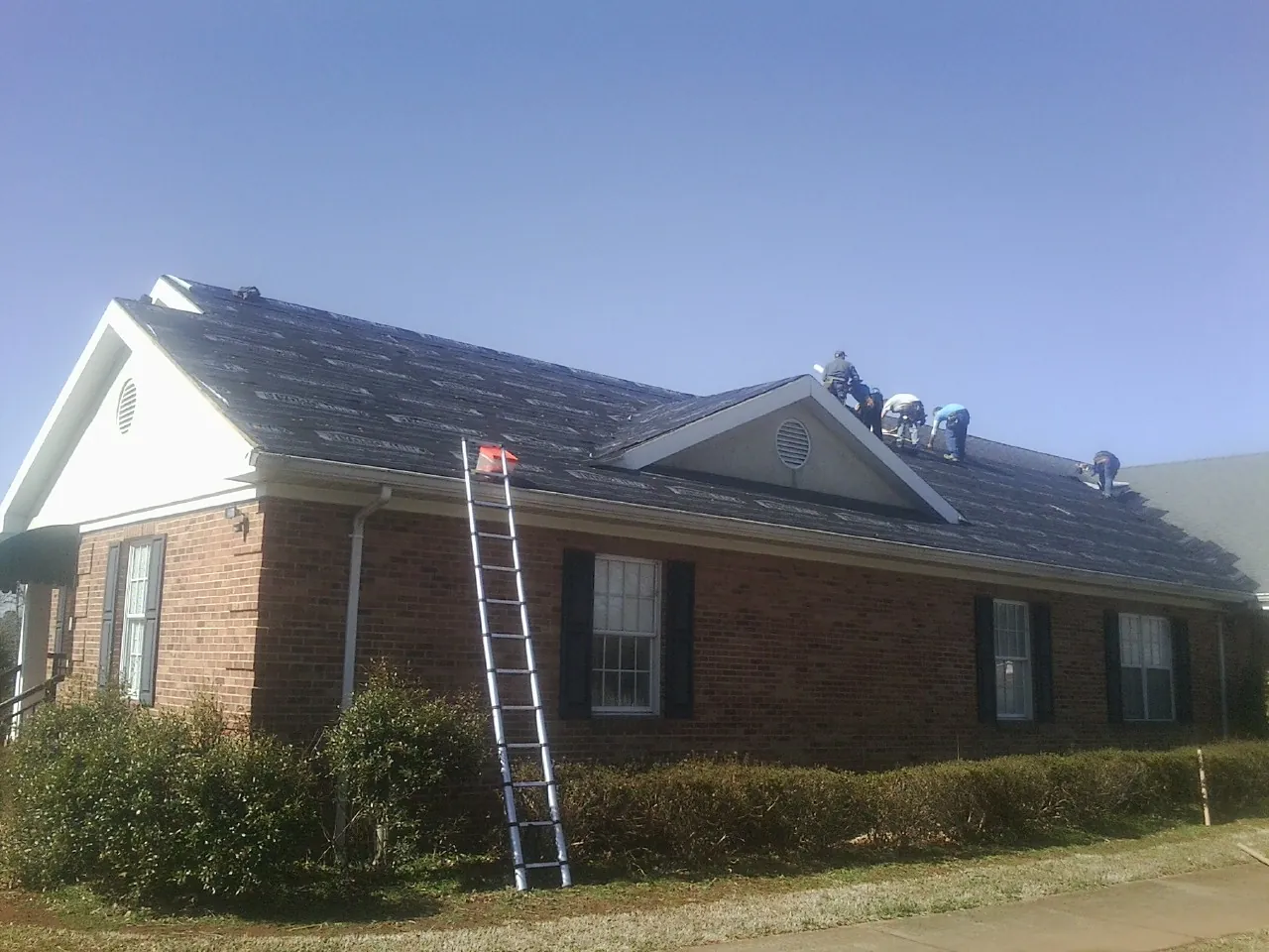 Crew tearing shingles off a brick ranch roof with a ladder set — Emergency Roof Repair work by our crew in Aguanga