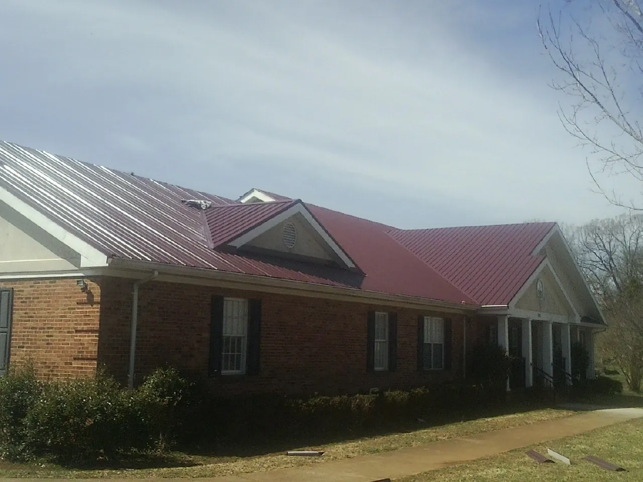 Red metal roof with gabled entries on a long brick building, from a Hail Damage Roof Repair job in Aguanga