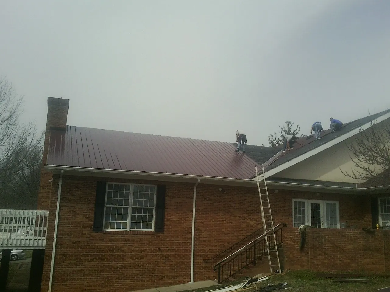 Crew setting red metal roofing panels on a brick home in Aguanga