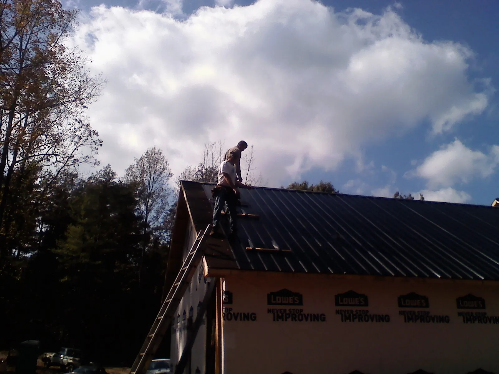 Roofer fastening dark metal panels high against a cloudy sky, from a Roof Inspection job in Aguanga
