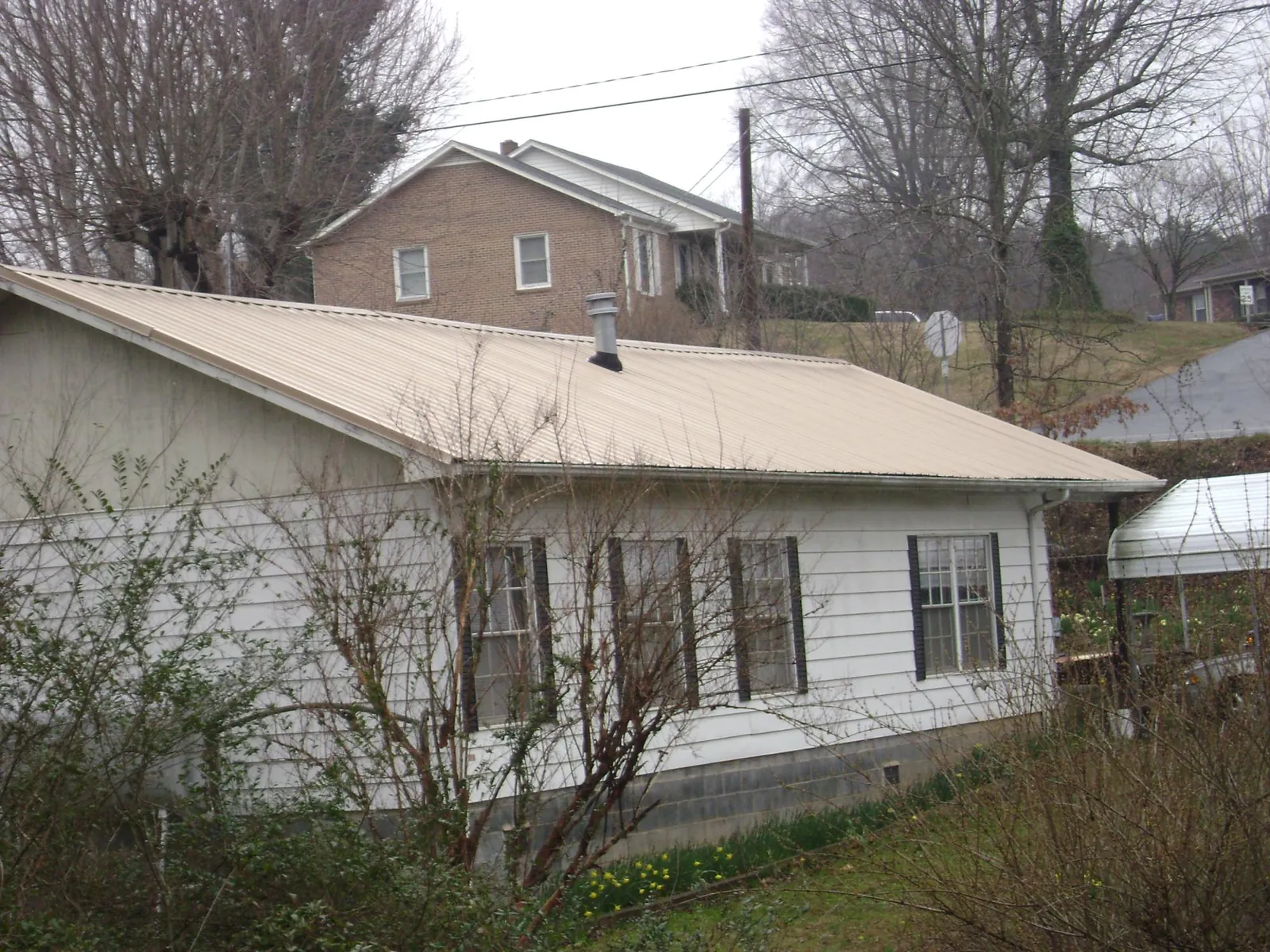 Tan metal roof on a white sided house set into a hillside — Commercial Roofing by Roofing Brothers in Aguanga